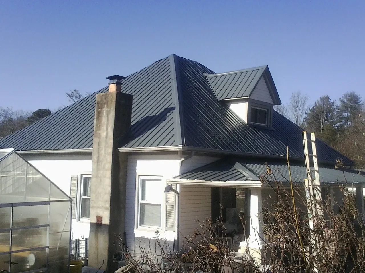 Dark blue standing seam metal roof on a white farmhouse with dormer — Slate & Tile Roof Repair by Roofing Brothers in Natick