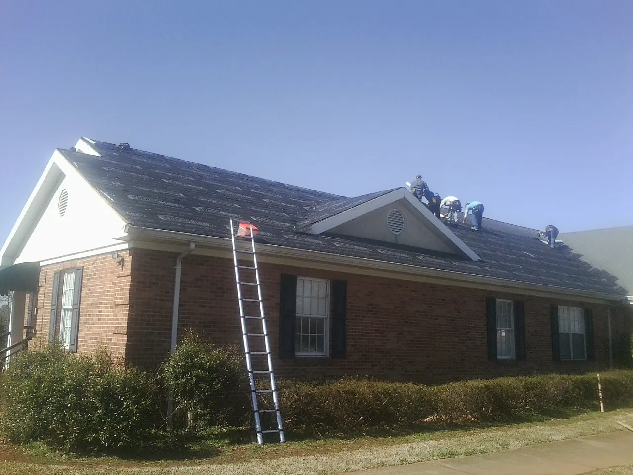 Crew tearing shingles off a brick ranch roof with a ladder set — Emergency Roof Repair work by our crew in Natick