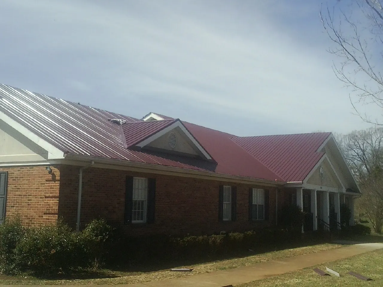 Red metal roof with gabled entries on a long brick building, from a Hail Damage Roof Repair job in Natick