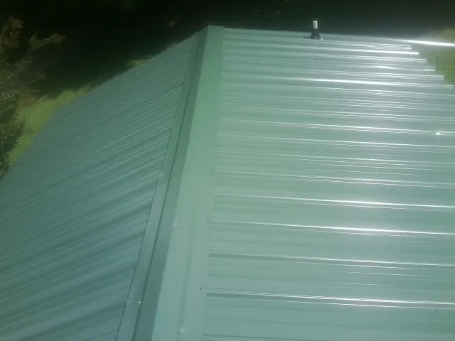New green metal panels meeting at the ridge of a roof — Flat Roof Repair work by our crew in Natick
