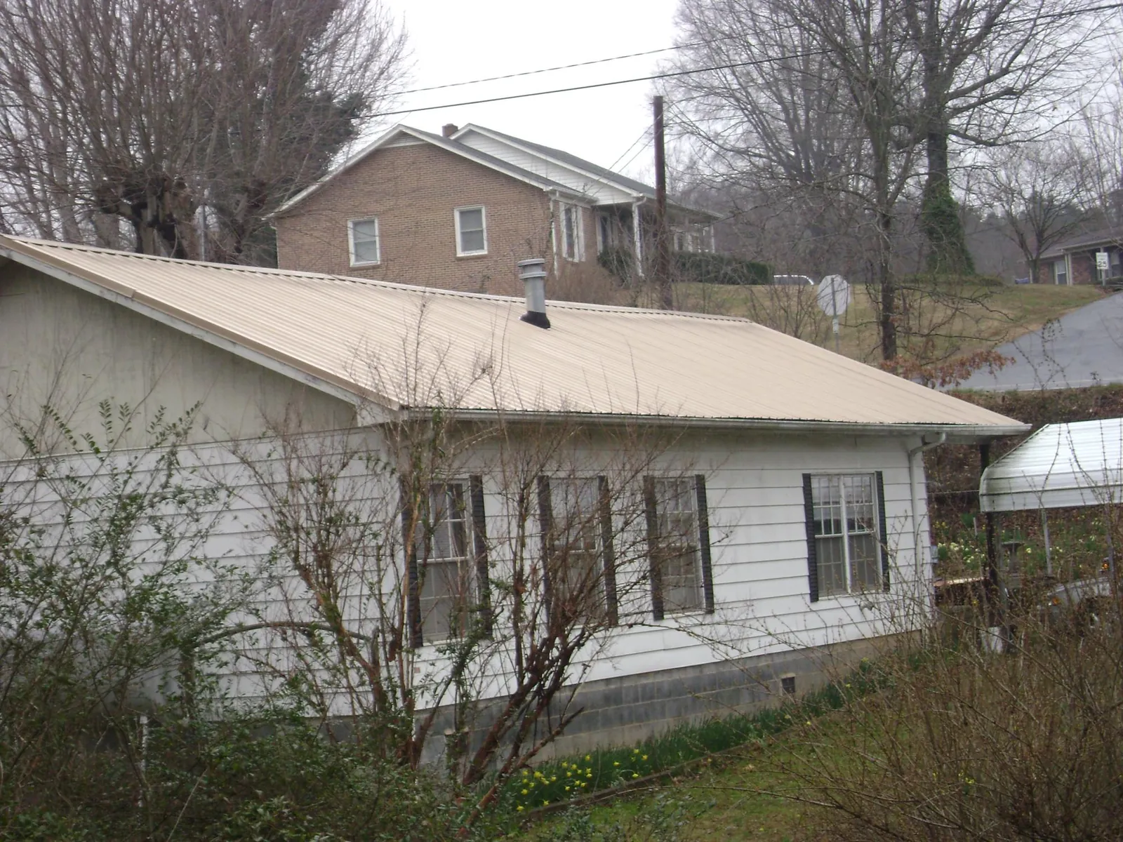 Tan metal roof on a white sided house set into a hillside — Commercial Roofing by Roofing Brothers in Natick