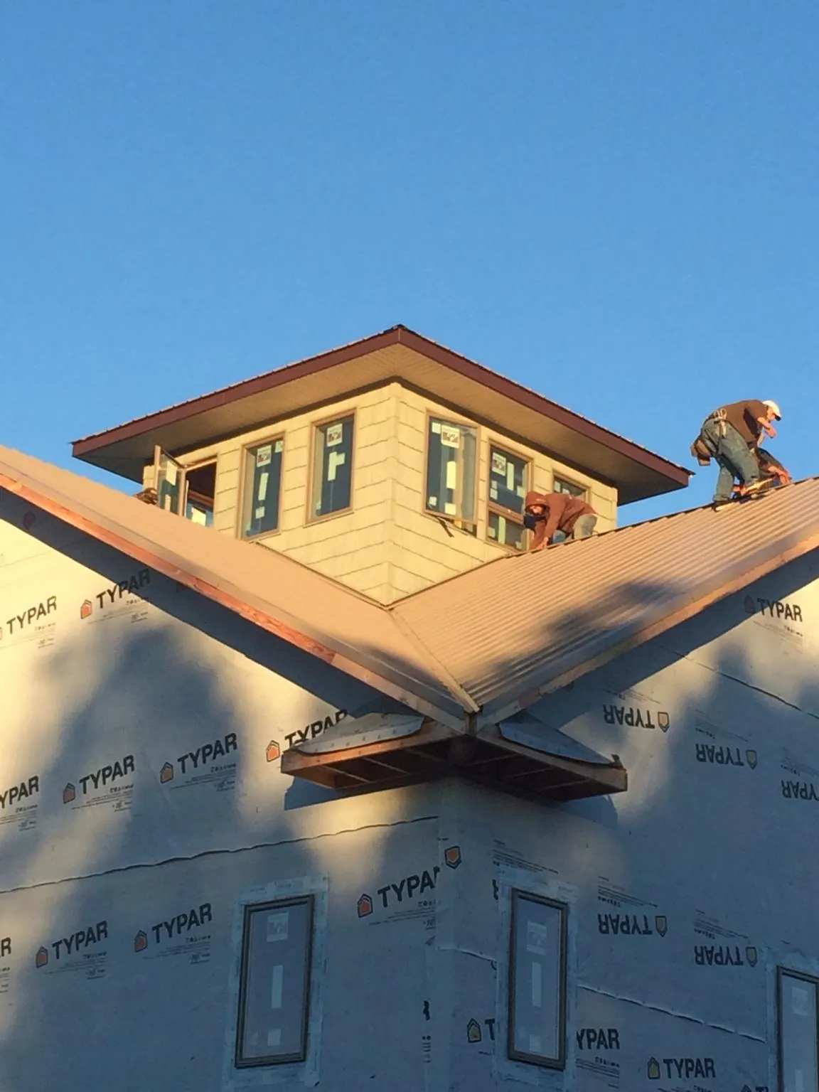 Roofers working around a rooftop cupola on a new metal roof at sunset — Roof Waterproofing in Natick by Roofing Brothers